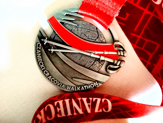 Zdjęcie przedstawia medal Czaniecki Cracovia Walkathon zawieszony na czerwonej taśmie z nazwą sponsora