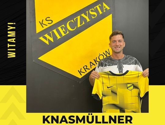 Na zdjęciu znajduje się nowy zawodnik Wieczystej Kraków Knasmüllner, trzyma w rękach koszulkę nowego klubu, a zanim pojawia się logotyp klubu piłkarskiego z Krakowa.